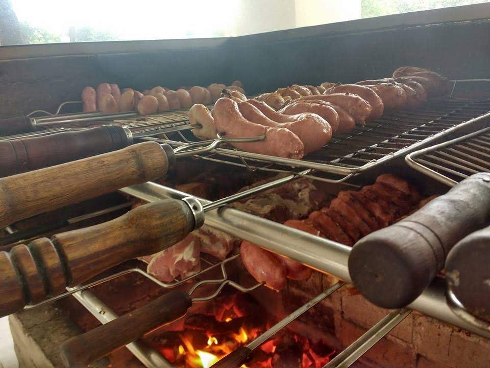 Churrasqueira de tijolos com espetos de linguiça e carnes sobre a brasa