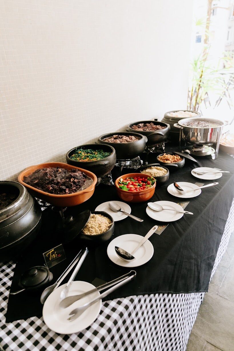 Feijoada completa servida em panelas de barro sobre mesa preta