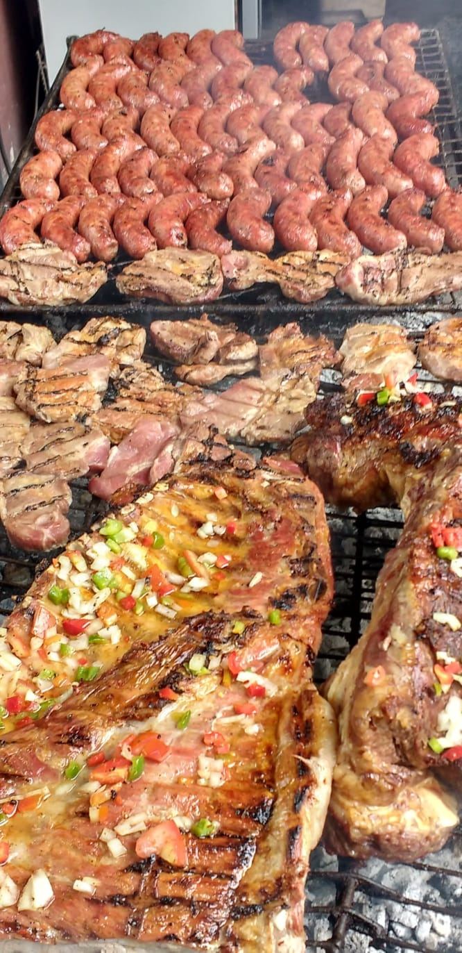 Grelha completa com linguiças, cortes de carne e legumes assando