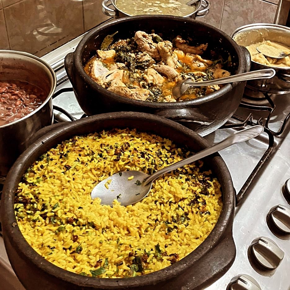Panelas de barro com arroz temperado, feijoada e frango ao molho em fogão industrial