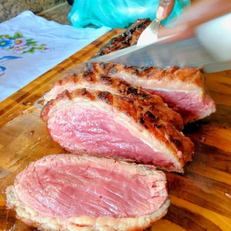 Picanha fatiada ao ponto, rosada por dentro, sendo cortada na tábua